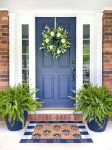 Door and Gate Decoration Ideas navy front door with brass hardware, an overhead sconce, and matching greenery planters.