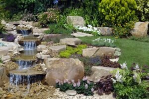 Small garden water feature and fountain surrounded by potted plants